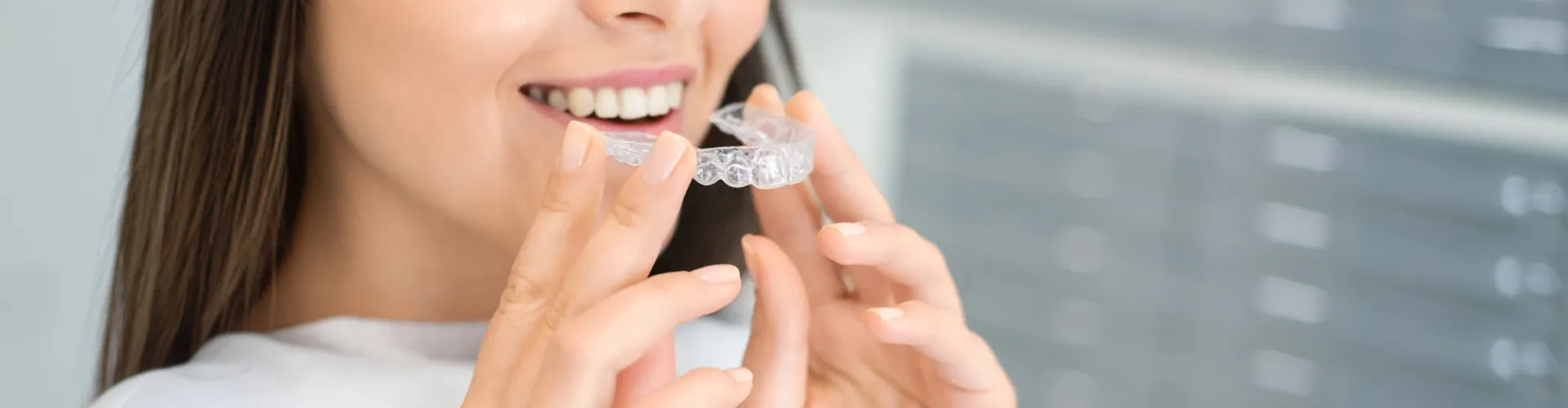 Woman placing clear aligner into her mouth.