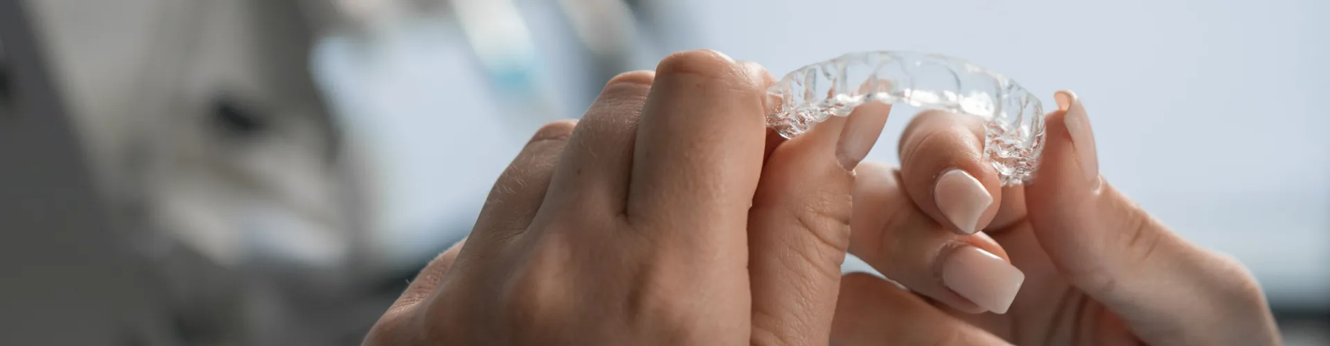 Close-up of hands holding a clear plastic Invisalign aligner for teeth straightening treatment.