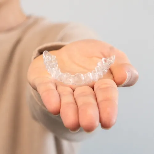 Person holding a clear orthodontic aligner in their open hand, highlighting a discreet option for straightening teeth.