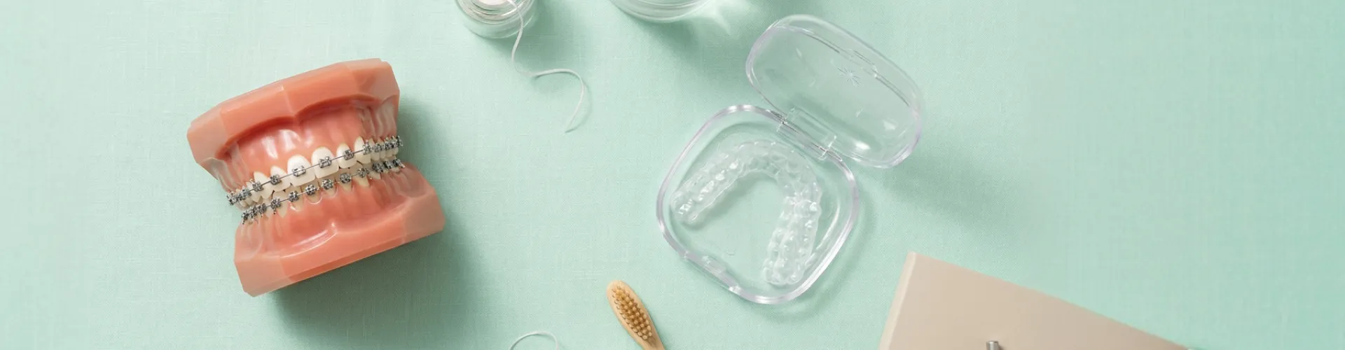 Dental model with metal braces and clear Invisalign aligner case on green background.