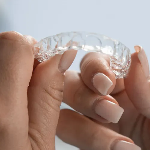 Close-up of hands holding a clear plastic Invisalign aligner for teeth straightening treatment.