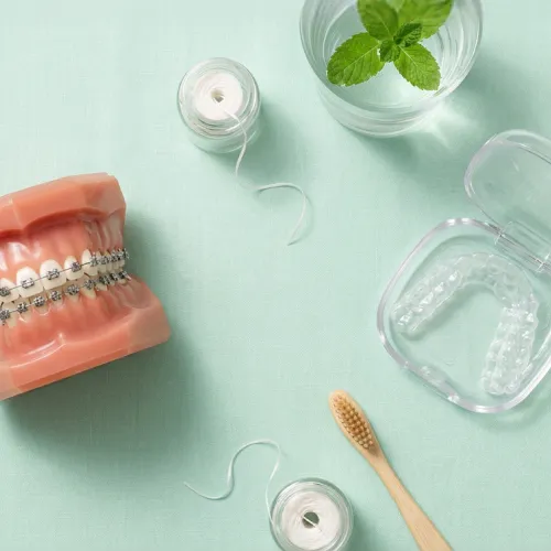 Dental model with metal braces and clear Invisalign aligner case on green background.