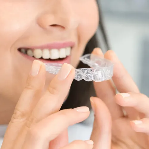 Woman placing clear aligner into her mouth.