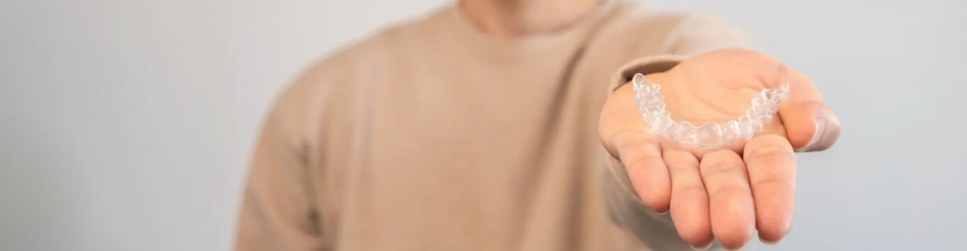 Person holding a clear orthodontic aligner in their open hand, highlighting a discreet option for straightening teeth.